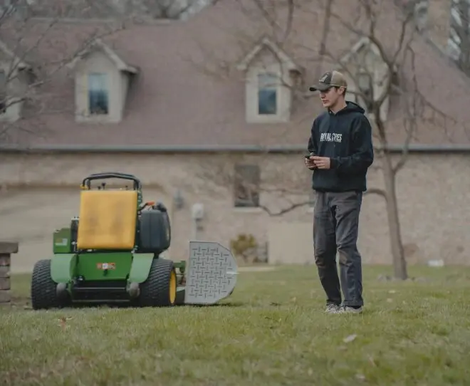 A Royal Acres mower on a lawn, with a crew member standing beside it